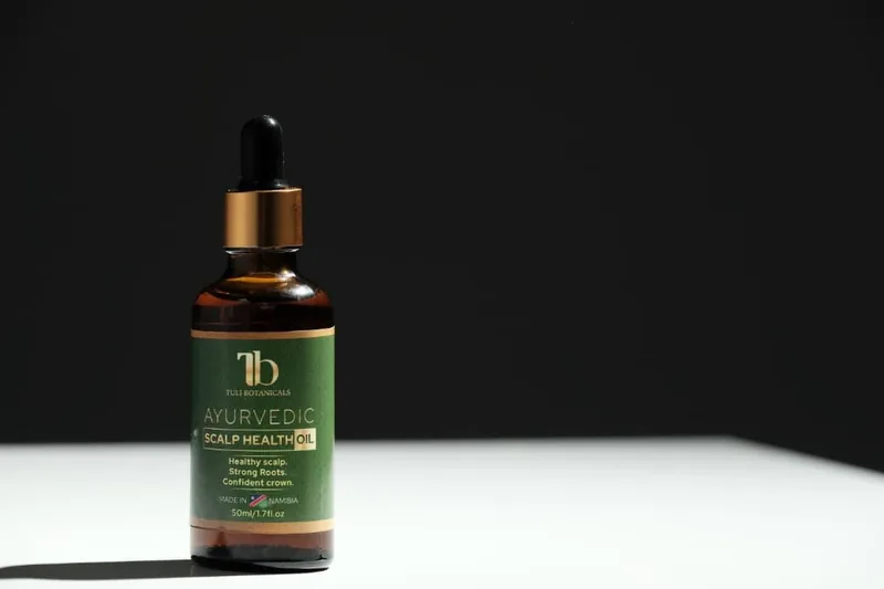 Amber glass bottle of Tuli Botanicals Ayurvedic Scalp Health Oil on a white table against a dark background.